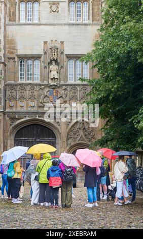 Turisti cinesi con ombrelloni fuori dall'ingresso principale del Trinity College, Università di Cambridge, Inghilterra, in una giornata umida e piovosa. Foto Stock