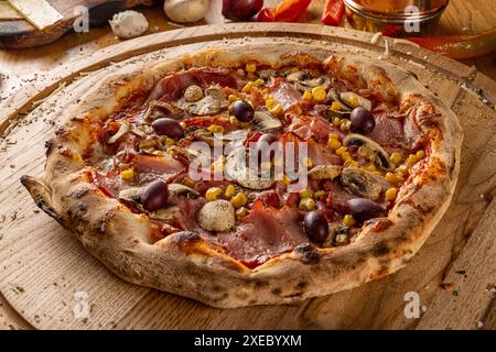 Pizza capriciosa, pizza classica con prosciutto, funghi, mais e olive su tavola di legno. Pizza italiana tradizionale. Foto Stock