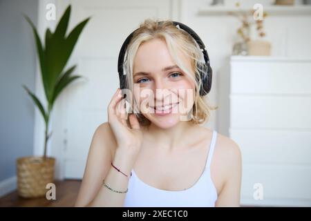 Ritratto di una giovane donna bionda dall'aspetto accattivante con le cuffie wireless, ascolta podcast o canzoni preferite e ascolta la musica con un nuovo orecchio Foto Stock