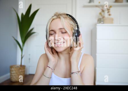 Concetto di persone e stile di vita, primo piano di una bella donna bionda con le cuffie wireless, ascolta musica e gode di buona qualità Foto Stock