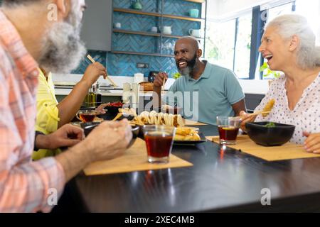 A casa, diversi gruppi di amici anziani si godono il pasto e ridono insieme in cucina Foto Stock