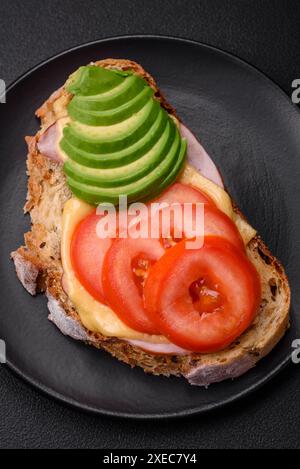 Delizioso e nutriente toast alla griglia con prosciutto, formaggio, pomodori e avocado Foto Stock