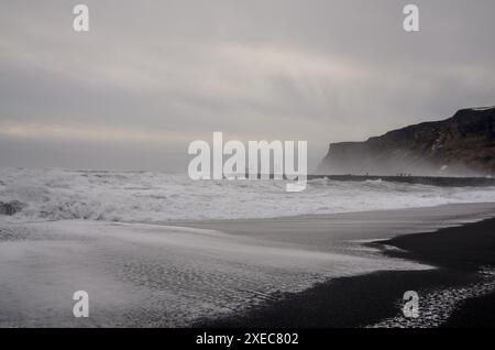Il mare scorre sulle sabbie nere della spiaggia di Vikurfjara, vicino a Vik, nella Terra del fuoco e del ghiaccio, in Islanda. Reynisdrangar è visibile sullo sfondo Foto Stock