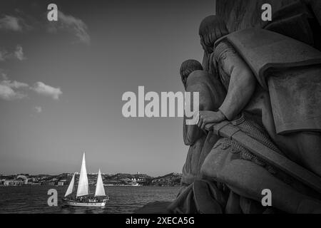 Vista in bianco e nero di una barca a vela passando accanto al Monumento alle scoperte sul fiume Tago - Lisbona, Portogallo Foto Stock