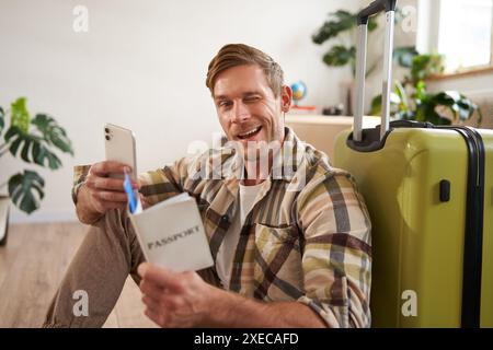 Giovane carismatico, viaggiatore in vacanza, viaggio all'estero, seduta con valigia, smartphone, biglietti e passaporto, Foto Stock