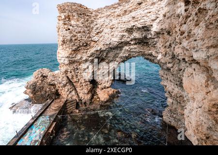 Un grande arco di roccia con una piccola piscina d'acqua di fronte. L'acqua è calma e il cielo è limpido. Foto Stock