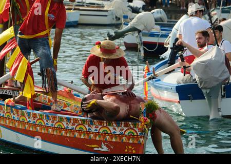 ACI TREZZA, ITALIA - 24 GIUGNO 2024 - Festa tradizionale di San Giovanni. Sfilata tradizionale di San Giovanni con pisci a mari dove riproducono la caccia al tonno. Il tonno viene derubato da un giovane che finalmente riesce a fuggire dai pescatori Foto Stock