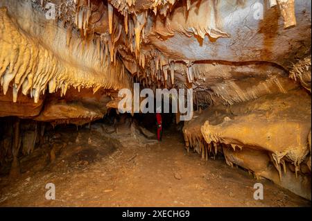 Uno speleologo con casco e faro che esplora una grotta con ricche formazioni di stalattiti e stalagmiti. Foto Stock