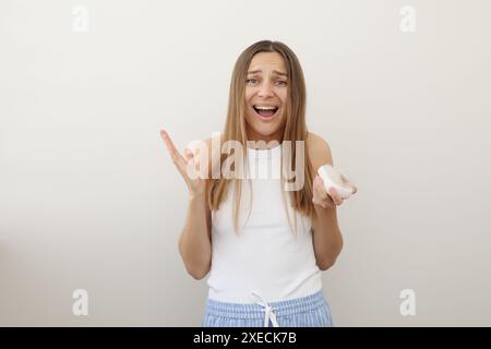 Problema di perdita dei capelli. Una giovane donna che urla tiene la spazzola per capelli con un mucchio di capelli caduti dopo la pettinatura. Periodo postpartum, alopecia, sintomi di disturbo endocrino, squilibrio ormonale, concetto di stress Foto Stock