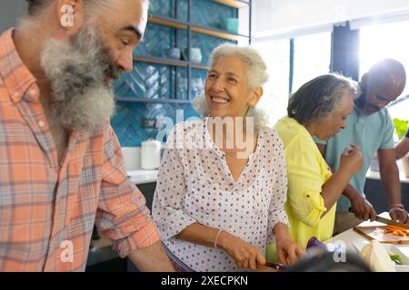 A casa, diversi gruppi di amici anziani cucinano insieme, godendosi del tempo in cucina Foto Stock