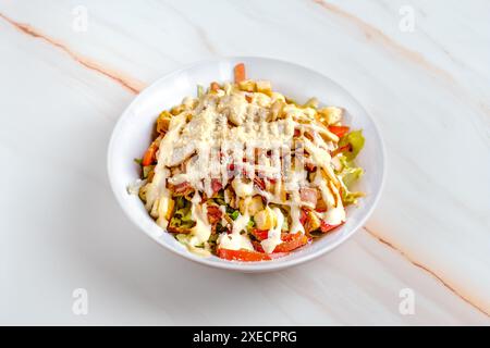 Una vivace insalata Caesar condita con pancetta croccante, crostini croccanti e condimento cremoso, servita in una ciotola bianca su un ripiano in marmo. Foto Stock