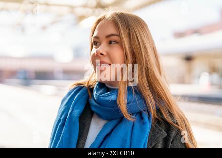 Ritratto di donna con una valigia gialla in attesa di un treno alla stazione ferroviaria sul binario. Concetto di stile di viaggio. Foto Stock