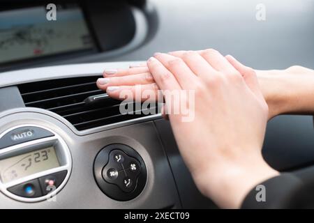La donna riscalda le mani sull'uscita dell'aria calda dell'auto. Mani fredde. Foto Stock
