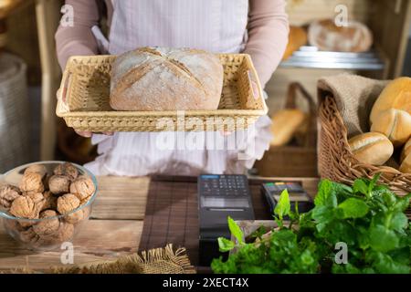 Una donna sta tenendo una pagnotta di pane appena sfornato su un tavolo di legno in un cestino intrecciato. Panetteria per famiglie multigenerazione Foto Stock