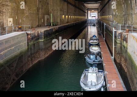 Storica base sottomarina tedesca della seconda guerra mondiale situata a Lorient, Bretagna, Francia. Presenta vecchie barche ancorate lungo un canale lungo e stretto. Foto Stock