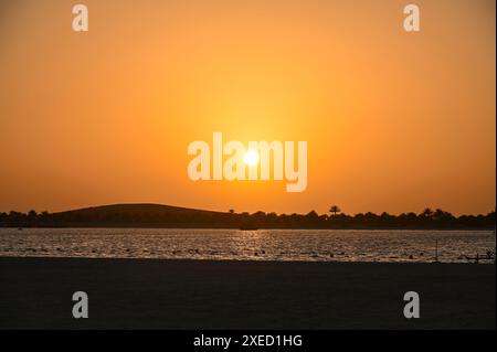 Tramonto sul deserto e Abu Dhabi con sagome di mare e palme, paesaggio come sfondo Foto Stock