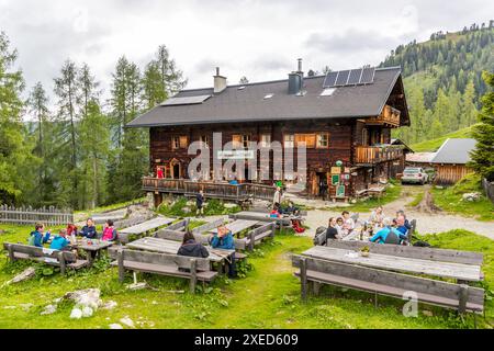 Il Filzmoosalm, a 1.710 metri nella valle di Großarl, offre pasti e pernottamenti sul sentiero degli alpi di Salisburgo, Salisburgo, Austria. Gli escursionisti siedono su panche di legno sulla terrazza del rifugio in legno a due piani, il cui tetto è dotato di pannelli solari. Foto Stock