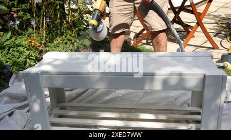 Uomo che dipinge mobili da giardino in legno con una pistola a spruzzo Foto Stock