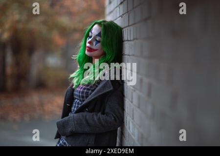 Ritratto di una ragazza con capelli verdi in abito da masticare con trucco joker su una parete di mattoni sfondo sfocato. Foto Stock