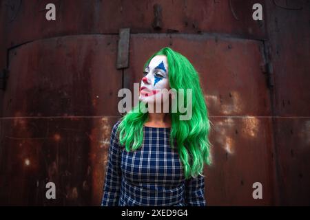 Ritratto di una ragazza con capelli verdi in abito da masticare con trucco joker su un ambiente atmosferico arrugginito parete di metallo. Foto Stock