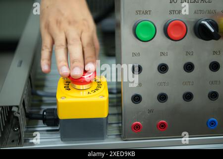 Primo piano della mano premendo il pulsante STOP sul pannello di controllo di una macchina industriale. Foto Stock