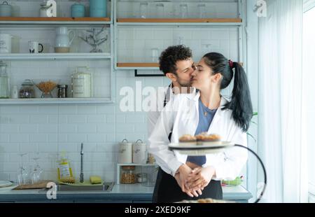 Un marito indossa un grembiule mentre cucina la cena con sua moglie. Ha abbracciato sua moglie felicemente prima di andare in cucina a cucinare. Foto Stock