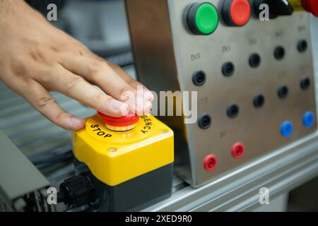 Primo piano della mano premendo il pulsante STOP sul pannello di controllo di una macchina industriale. Foto Stock