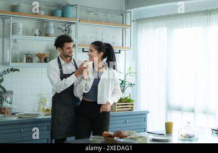 Un marito indossa un grembiule mentre cucina la cena con sua moglie. Ha abbracciato sua moglie felicemente prima di andare in cucina a cucinare. Foto Stock