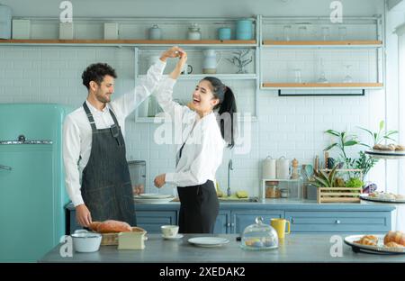 Un marito indossa un grembiule mentre cucina la cena con sua moglie. Stava ballando felicemente prima di entrare in cucina per cucinare. Foto Stock