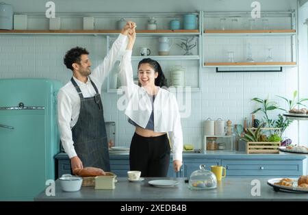 Un marito indossa un grembiule mentre cucina la cena con sua moglie. Stava ballando felicemente prima di entrare in cucina per cucinare. Foto Stock