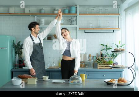 Un marito indossa un grembiule mentre cucina la cena con sua moglie. Stava ballando felicemente prima di entrare in cucina per cucinare. Foto Stock