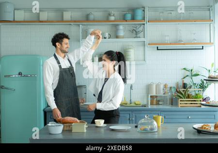 Un marito indossa un grembiule mentre cucina la cena con sua moglie. Stava ballando felicemente prima di entrare in cucina per cucinare. Foto Stock