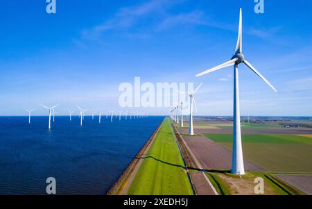 Un paesaggio sereno in cui una fila di turbine eoliche si erge alto accanto a un tranquillo specchio d'acqua nel Flevoland olandese Foto Stock