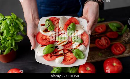 La donna tiene l'insalata caprese sul piatto, primi piani di pomodori e mozzarella Foto Stock