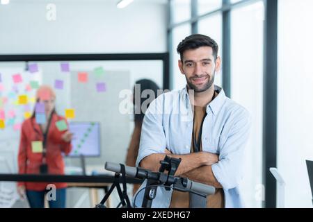 Ritratto di un uomo d'affari sorridente che guida uno scooter elettrico in ufficio con un collega sullo sfondo Foto Stock