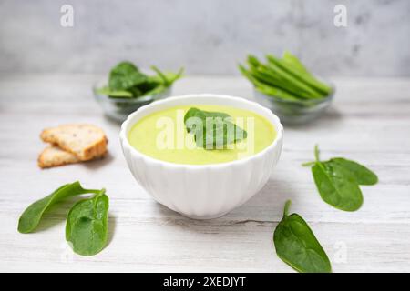 Zuppa fatta in casa con panna di spinaci in un recipiente bianco con pane su sfondo bianco in legno. Cibo dietetico. Foto Stock