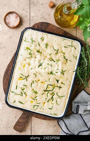 Impasto di focaccia crudo all'interno del piatto da forno con ingredienti, olio d'oliva e basilico su un vecchio tavolo rustico. Processo di preparazione della focaccia con impasto naturale. Trad Foto Stock