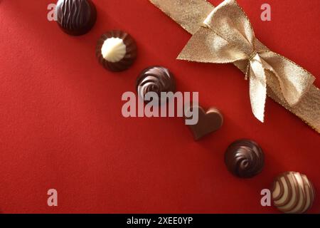 Fila di cioccolatini assortiti e arco regalo dorato isolato su un tavolo rosso. Vista dall'alto. Foto Stock