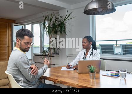 Giovane uomo visita donna medico in ufficio medici, avendo problemi di salute con dolore, parlare con il medico generico in cappotto bianco con stetoscopio a. Foto Stock