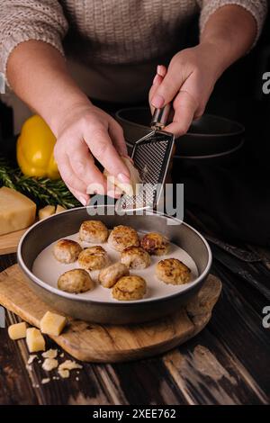 donna che grattugia il parmigiano sulle polpette in salsa panna Foto Stock