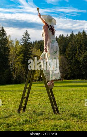 Una donna su una scala di legno dipinge il cielo blu Foto Stock