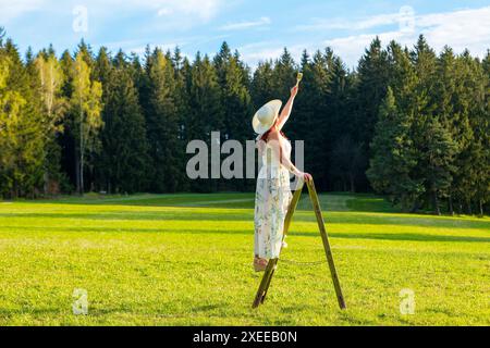 Una donna su una scala di legno dipinge il cielo blu Foto Stock