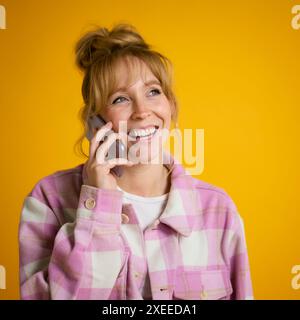 Donna sorridente con naso Piercing che parla al telefono cellulare sullo sfondo di Yellow Studio Foto Stock