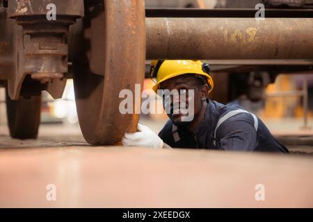 Il tecnico ferroviario in uniforme e con casco ispeziona le ruote del treno rimosse dalle locomotive nell'officina ferroviaria. Foto Stock