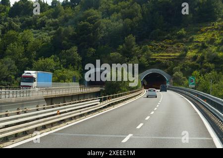 Imperia, Italia - 12 maggio 2023: Un'ampia autostrada con due corsie, una per ogni direzione, si estende attraverso un versante boscoso. La strada ha un ponte Foto Stock