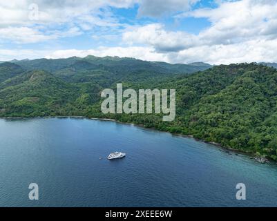 Una piccola barca subacquea si ferma all'ancora lungo la costa di una remota isola tropicale in Indonesia. Questa regione ospita una grande biodiversità marina. Foto Stock