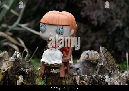 Funko Pop action figure della bambola vintage infestata Annabelle dei film soprannaturali di Conjuring. Moody, cupo, spettrale, foresta verde scuro, ceppo di alberi. Foto Stock