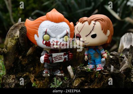 Figure Funko Pop tratte da film horror. Il clown malvagio Pennywise e la bambola del serial killer Chucky. Moody, cupo, spettrale, foresta verde scuro, ceppo di alberi. Foto Stock