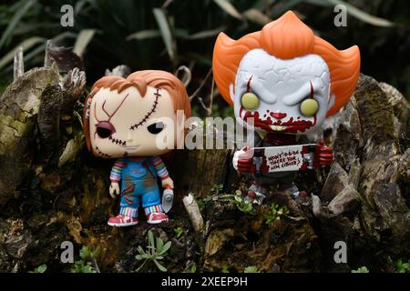 Figure Funko Pop tratte da film horror. Il clown malvagio Pennywise e la bambola del serial killer Chucky. Moody, cupo, spettrale, foresta verde scuro, ceppo di alberi. Foto Stock