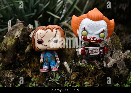 Figure Funko Pop tratte da film horror. Il clown malvagio Pennywise e la bambola del serial killer Chucky. Moody, cupo, spettrale, foresta verde scuro, ceppo di alberi. Foto Stock